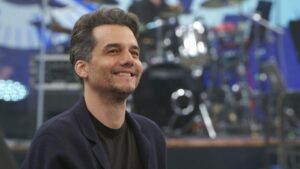 A foto mostra o ator Wagner Moura. Um homem branco, cabelo escuro, usando camiseta e jaqueta.