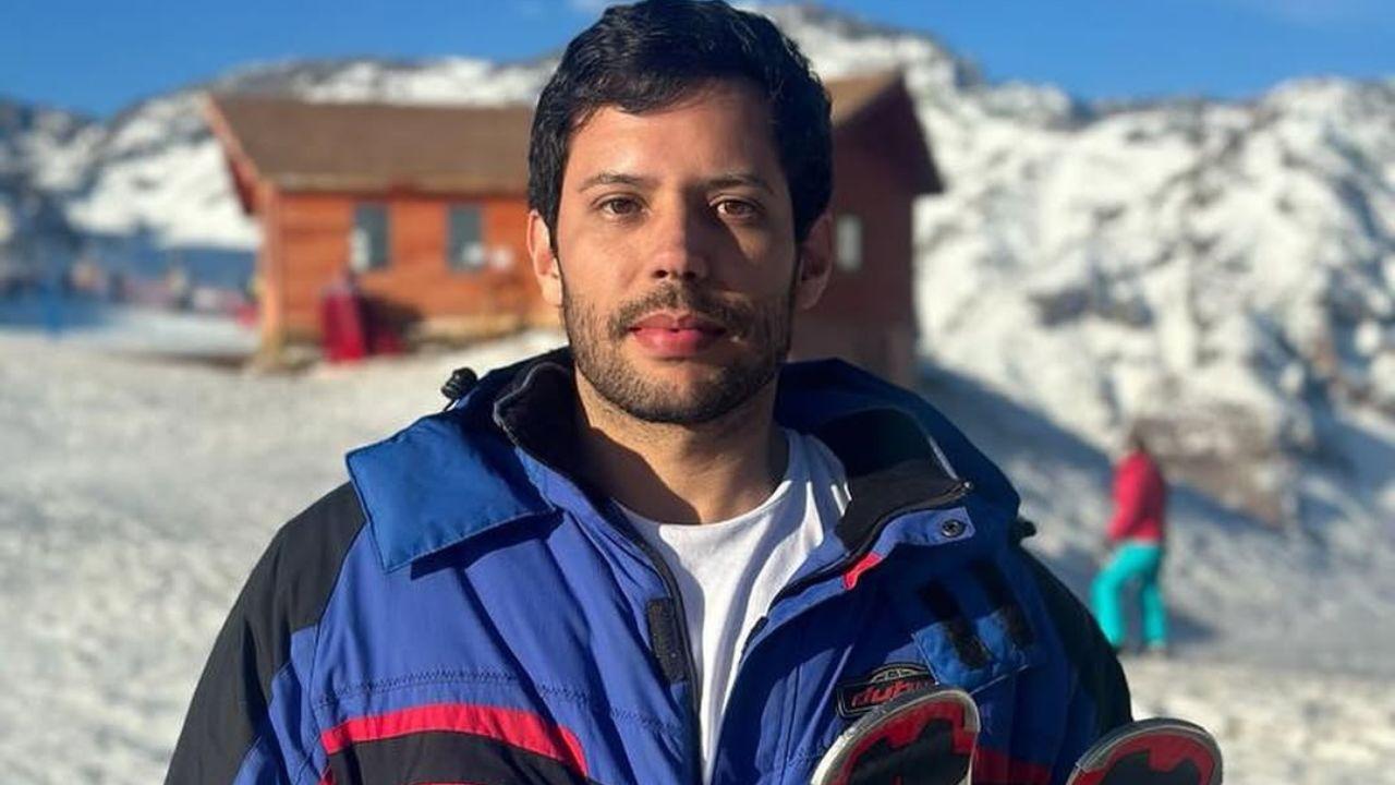 Homem branco, cabelo castanho curto, homem com barba e ao fundo tem neve. Ele usa roupas de neve.