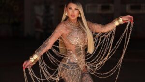 Andressa Urach. Mulher branca, loira, cabelo liso longo, fantasia de correntes douradas.