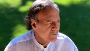 Homem branco, idoso, calvo, com camisa branca ao ar livre.