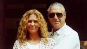 Mulher branca, loira, cabelo cacheado e homem branco de óculos.
