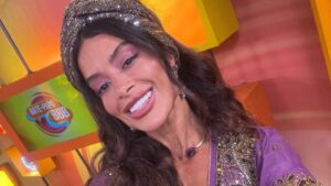 Aline Campos. Mulher branca, cabelo castanho, liso, com lenço cinza na cabeça, camisa roxa larga.