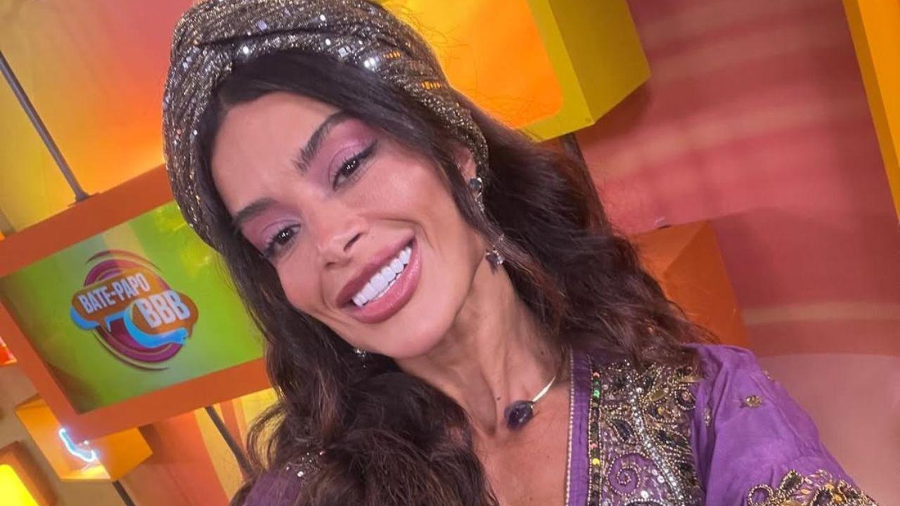 Aline Campos. Mulher branca, cabelo castanho, liso, com lenço cinza na cabeça, camisa roxa larga.