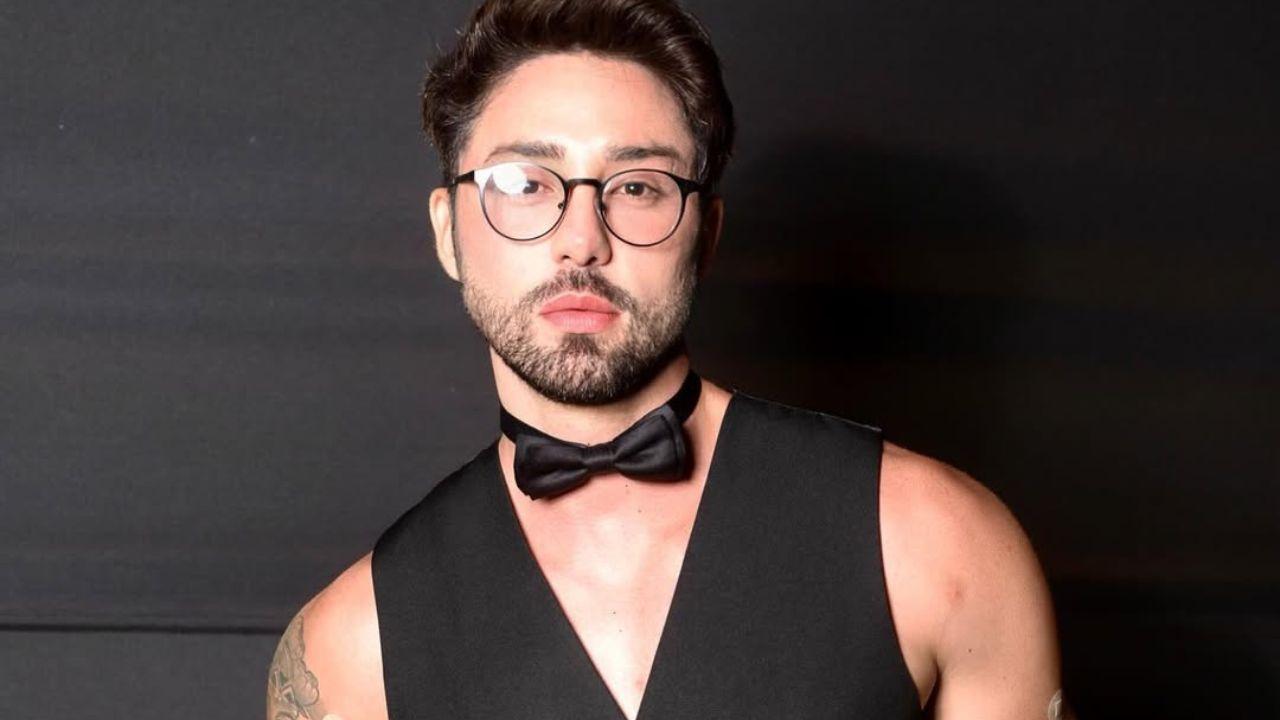 Rico Melquiades. Homem branco, cabelo preto curto, de óculos, colete e gravata preto.