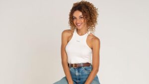 Atriz Gabriela Loran. Mulher negra, cabelo cacheado preso, usa blusa branca e calça jeans.