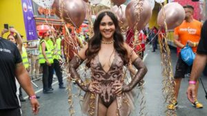 Alessandra Negrini. Mulher branca, cabelo castanho escuro médio com fantasia de carnaval marrom brilhante.
