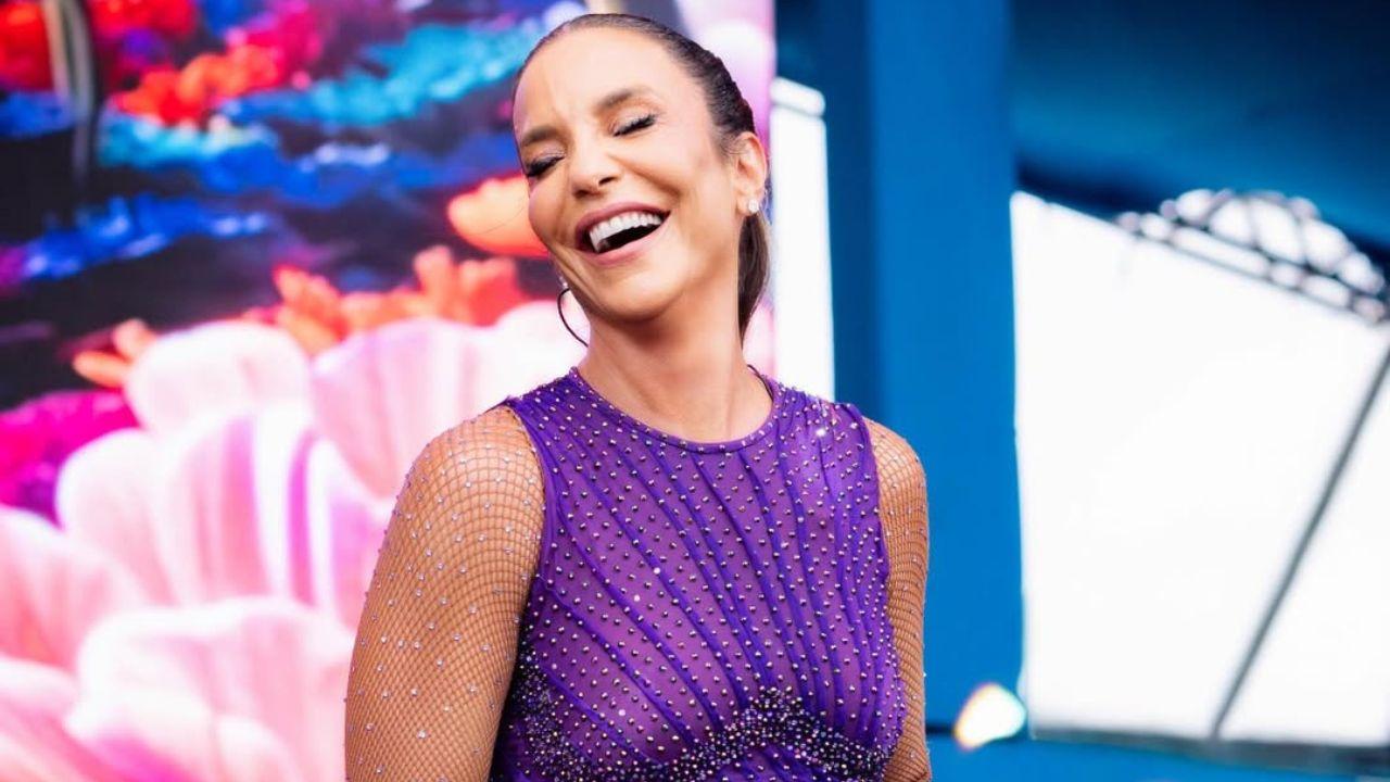 Ivete Sangalo com vestido roxo e cabelo preso cantando no palco.