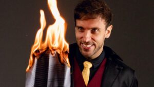 Leo Lins queimando um papel com rosto esquisito.