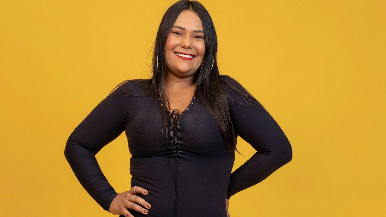 Chaiany do BBB. Mulher negra, cabelo preto liso, usando roupa preta em um fundo amarelo.