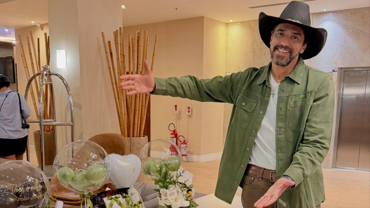 Cowboy usando jaqueta jeans verde e chapéu dentro de um hotel.