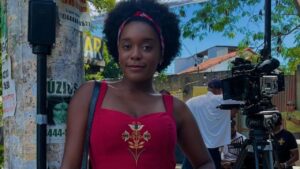 Atriz Luiza Rosa. Mulher negra, cabelo crespo, usando um vestido vermelho.
