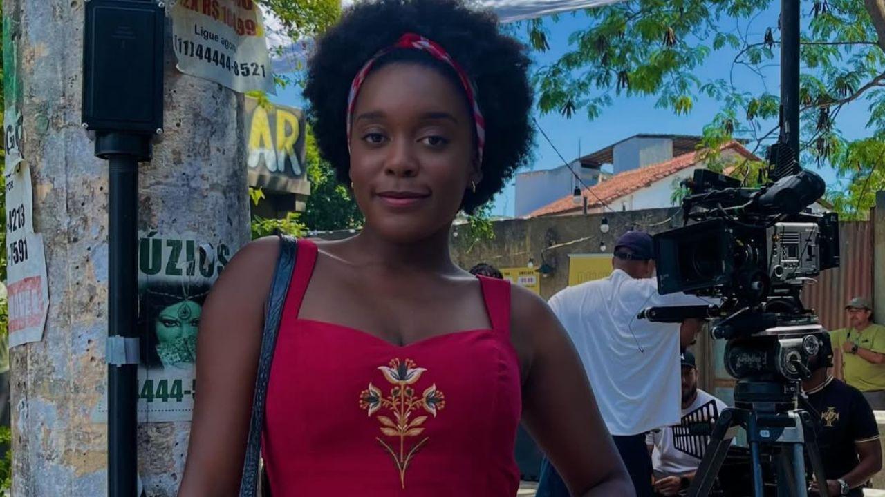 Atriz Luiza Rosa. Mulher negra, cabelo crespo, usando um vestido vermelho.