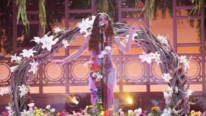 Anitta cantando no palco decorado com plantas e galhos de árvores.