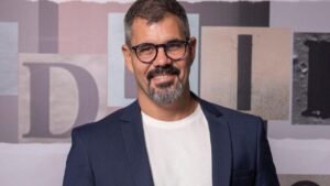 Ator Juliano Cazarré. Homem branco, com barba grisalha e óculos.