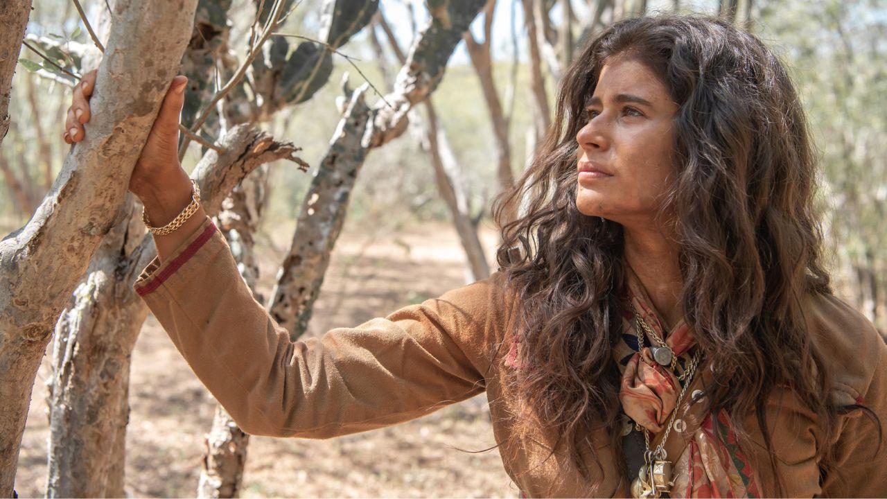 Foto da atriz Isadora Cruz. Ela está no sertão nordestino olhando para uma árvore.