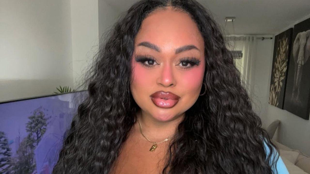 Rízia Cequeira. Mulher negra, cabelo cacheado longo, com lábios grandes e blusa azul.