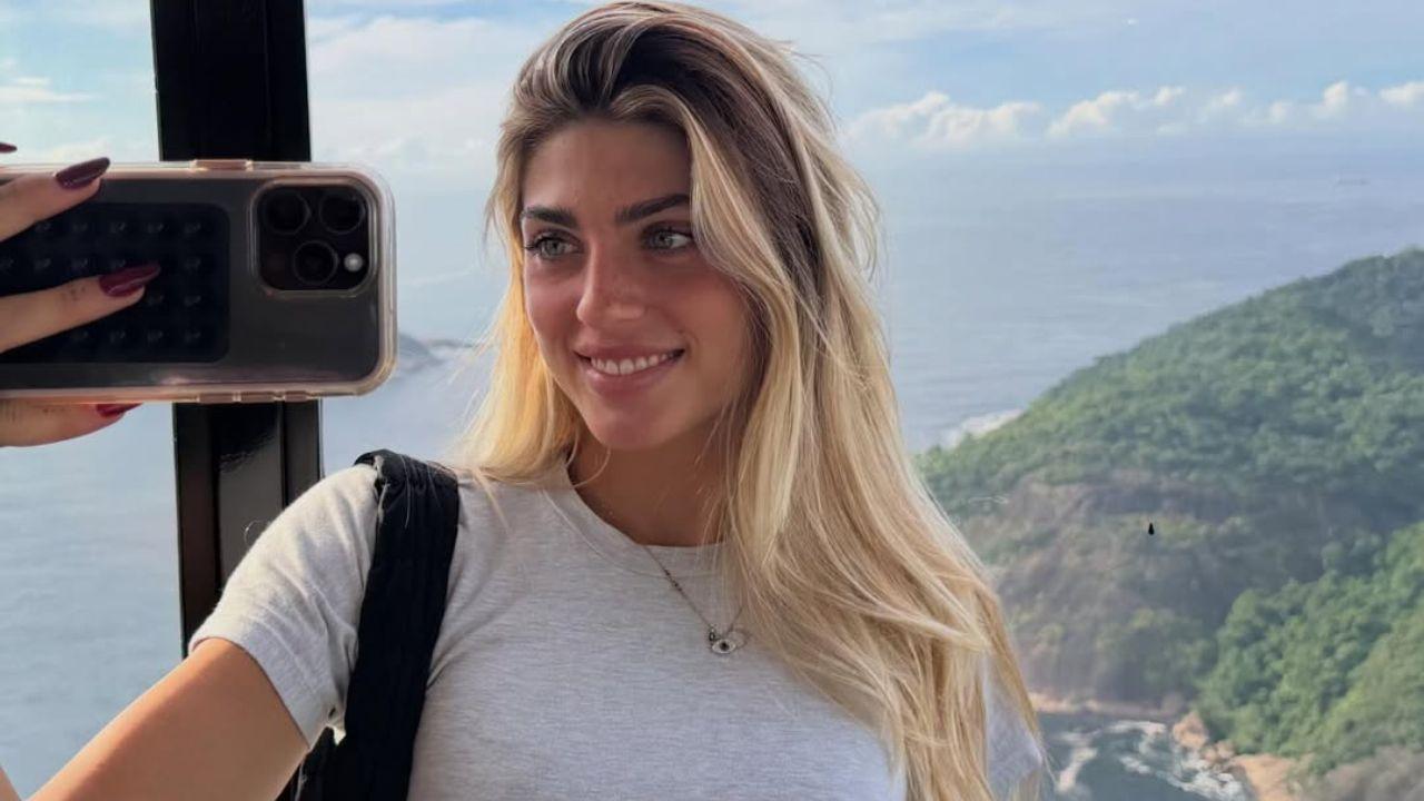 Modelo Manu Howlett. Mulher branca, loira, olhos claros, camiseta cinza.