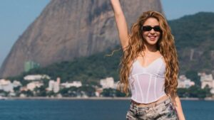 Shakira com corset branco, calça estampada, sorrindo na frente do morro do pão de açucar.