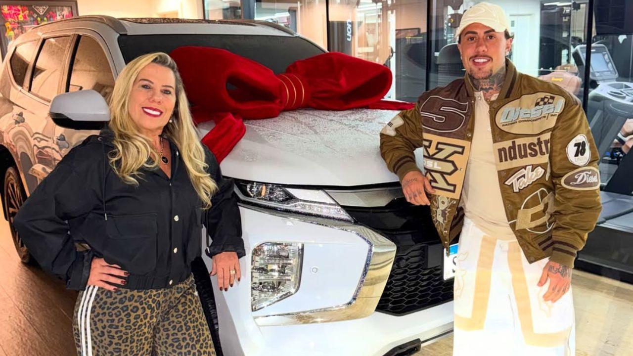 Mostra o cantor MC Daniel e a mãe dele ao lado de um carro de luxo.