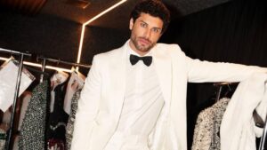 Modelo Jesus Luz de terno branco. Homem branco, cabelo cacheado curto, olho claro.