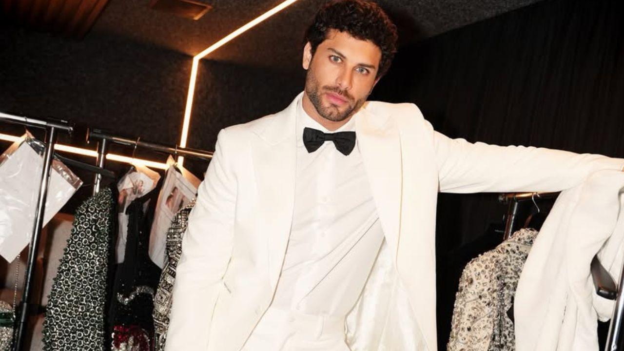 Modelo Jesus Luz de terno branco. Homem branco, cabelo cacheado curto, olho claro.