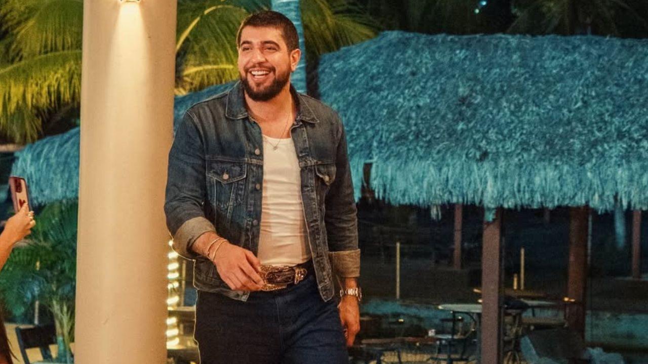 Cantor Nattan. Homem branco, cabelo preto curto, barba, camiseta branca e camisa jeans.