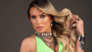Foto mostra Andressa Urach. Mulher loira, bem maquiada, usando blusa verde e joias douradas.