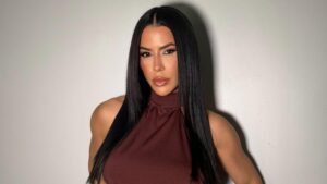 Larissa Tomásia. Mulher branca, cabelo liso longo, usando vestido marrom.
