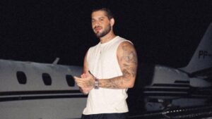 Zé Felipe. Homem branco, cabelo curto castanho, usando camiseta branca na frente de um avião.