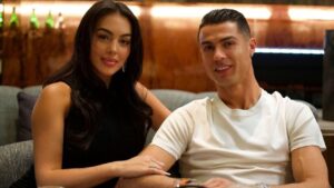 Cristiano Ronaldo e Georgina Rodríguez sentados no sofá sorrindo.