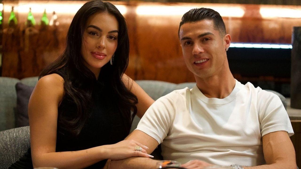 Cristiano Ronaldo e Georgina Rodríguez sentados no sofá sorrindo.