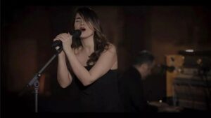 Cantora iraniana Parastoo Ahmadi. Mulher persa, cabelo liso castanho, usando vestido preto, cantando no palco.