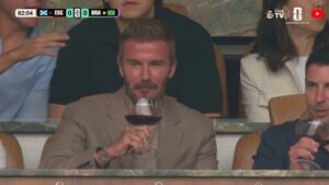 A foto mostra o jogador David Beckhan tomando vinho no camarote do estádio de futebol.