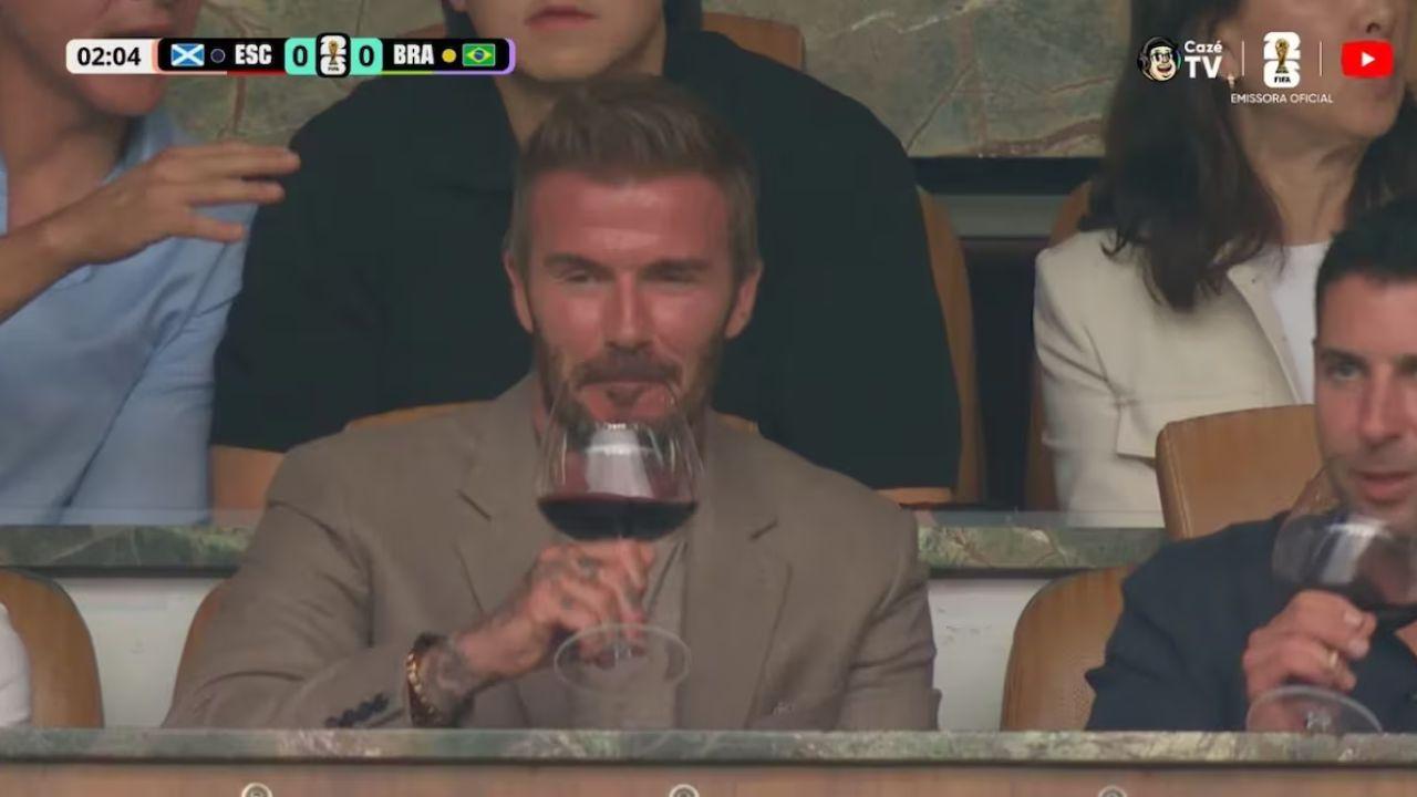 A foto mostra o jogador David Beckhan tomando vinho no camarote do estádio de futebol.