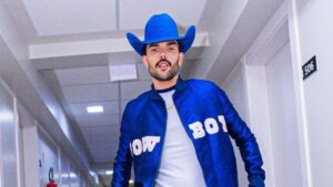 Foto mostra o cantor Luan Pereira. Homem branco, cabelo castanho e com barba, camiseta branca e casaco azul.