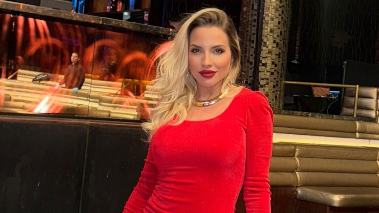 Clara Aguilar. Mulher branca, cabelo loiro, usando vestido e batom vermelho dentro de um cassino.