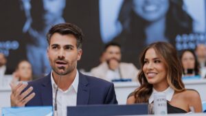 Foto mostra Adriana Sant'Anna e Rodrigão sentados numa mesa com um microfone na frente.