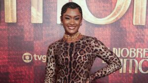 Atriz Erika Januza. Mulher negra, cabelo trançado, vestido de onça e sorrindo.