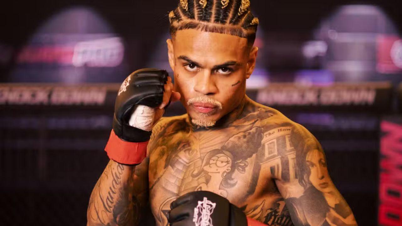 MC Cabelinho. Homem negro, de trança nagô, sem camisa, cheio de tatuagens, com luva de mma de luta.