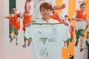 Foto mostra o filho do Neymar Davi Lucca. Menino jovem, branco, cabelo loiro, segurando uma bandeira do Instituto Neymar Jr.